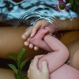 Cradling her feeding baby's feet during a floral bath.